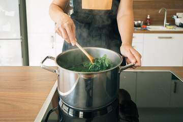 A person is cooking spinach in a pot, the pot is on the vitro ceramic cooktop