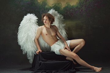Handsome man with curls and white wings posing radiates sense of peace looks as angel against...