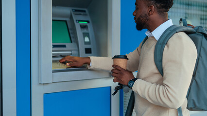 Man at ATM machine with a coffee cup