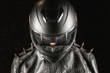 Brutal motorcyclist rider in black helmet and black studded leather jacket on a dark background.