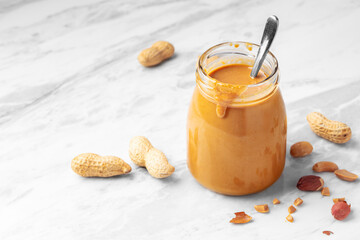 Natural peanut butter in glass jar with spoon on white marble table
