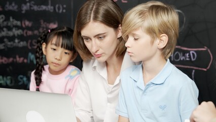 Young smart teacher using laptop to teach diverse student programing system. Caucasian learner...