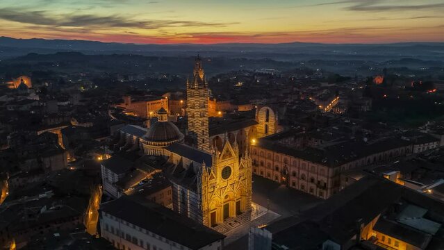 HDR 4K aerial shot of Siena with city lights, red sunrise sky at background. Fly over Siena, Tuscany, Italy early in the morning. Foggy hills at background