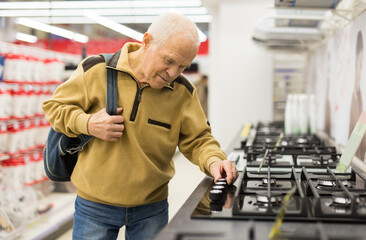 Elderly man choosing gas stove in showroom of electrical appliance store