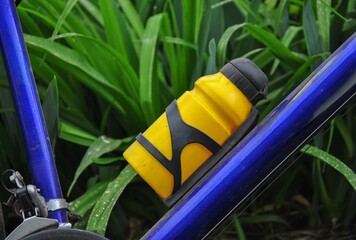 yellow bicycle water bottle on a bicycle close-up. green grass in the background. water bottle - obrazy, fototapety, plakaty