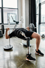 A man, with a prosthetic leg, lifting a barbell while doing a bench press in a gym.