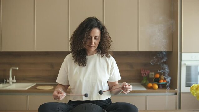 Relaxed curly brunette sitting in lotus pose on the kitchen table and playing tank drum