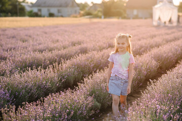 A smiling kid walks among lavender flowers with sunlight on a summer day. A child girl goes in a...