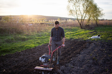 organic farming man ploughs the ground at sunset with a tiller preparing the soil for sowing