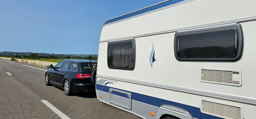 Car towing a caravan trailer on a freeway; automobile pulling a trailer camper on a quiet road in...