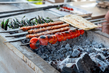 Traditional Adana kebabs with green peppers and tomatoe on bbq in a food festival, close up