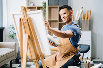 Asian male painter do artwork in art workshop, painting supplies, oil pastels, two canvas easel,...