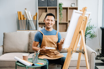 Asian male painter do artwork in art workshop, painting supplies, oil pastels, two canvas easel,...