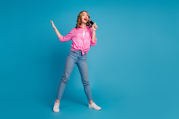 Full body photo of pretty young girl hold microphone singing wear trendy pink outfit hairdo isolated on blue color background