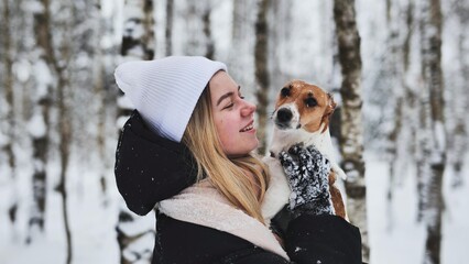 A girl cuddles a Jack Russell Terrier dog in the woods in winter.