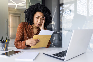 Focused African American woman looking concerned while reading a letter at her modern office...