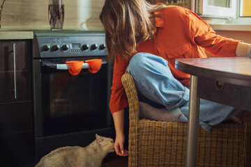 Beautiful young woman playing with a cat in the kitchen.