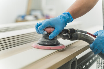 close-up hands of worker with gloves using electric sander in workshop. Joiner sanding wooden board...