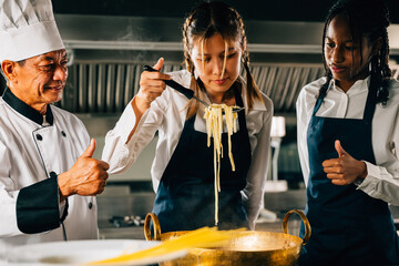 In kitchen chef mentors students. Schoolgirls create ramen. Kids and teacher at stove. Smiling...