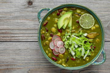 Vegan Pozole Verde dish with hominy, beans, tomatillo, and button mushrooms topped with avocado, radish, lime, and shredded napa cabbage. Copy space.