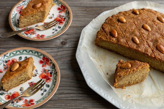Round cake with almonds, fenugreek seeds, and semolina and two plates with pieces of this cake. Sweet traditional helbeh (fenugreek cake) dessert. 