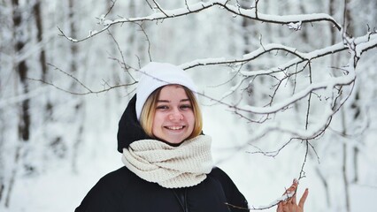 A girl gently touches snowy tree branches in the forest.