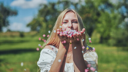 A girl blows a multi-coloured paper confetti out of her hands.