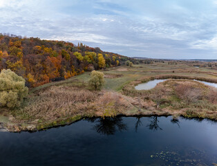 Aerial river valley panorama with colorful autumn forest and cloudy sky in Ukraine