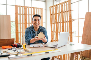 Portrait of a smile Asian male father sitting and working with a laptop on the table with the instrument of measure and working tools on the table at home woodwork studio.