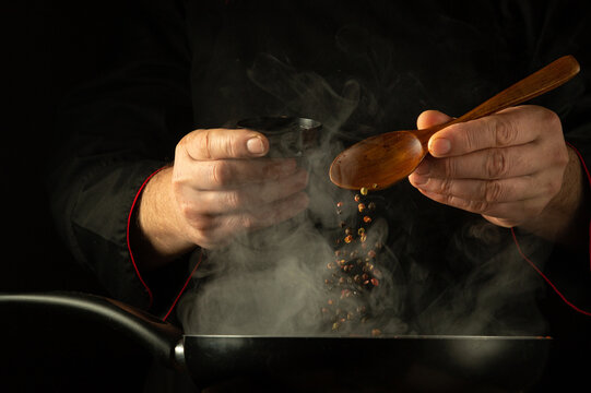 The chef adds dry pepper to the hot frying pan by hand. Low key concept of preparing a delicious lunch in a hotel kitchen. Grande cuisine
