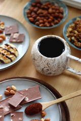 Cup of tea or coffee, cookies, macaroons, chocolate, various nuts and cocoa powder on wooden table. Selective focus.