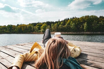 girl lying by the lake with a cup of coffee