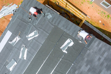 Roofing contractor uses air nail gun to install new asphalt bitumen shingles on roof house