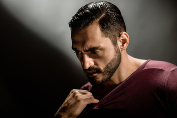 Fashion portrait of brutal strong guy with beard and trendy hairstyle, Intriguing depth: Portrait of a serious, young brunette man with a striking dark background