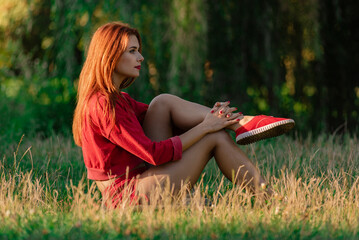 Portrait of young healthy fit woman sitting on grass after hard workout, Outdoor fitness session: forest workout for redhead girl.