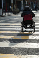 Obraz premium Person in a wheelchair crossing the road, copy space. Safe road traffic for people with disabilities.