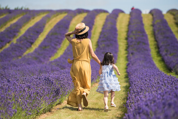 A mother wearing a yellow jumpsuit dress and a straw hat and her daughter wearing a blue dress hold...