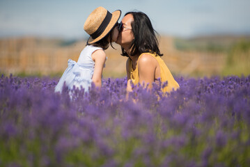 A young Asian mother wearing a yellow jumpsuit dress an sunglasses kissing her daughter while sitting in the middle of a lavender field in a sunny summer day in Kinross, Scotland, United Kingdom