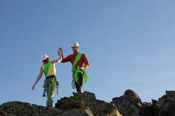 Two people are high on a mountain, one of them is wearing a green harness