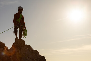 A man is standing on a rock with a green rope. The sun is shining brightly in the background