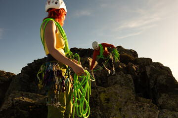 A woman in a yellow shirt is holding a green rope. A man is climbing up a rock with a green rope