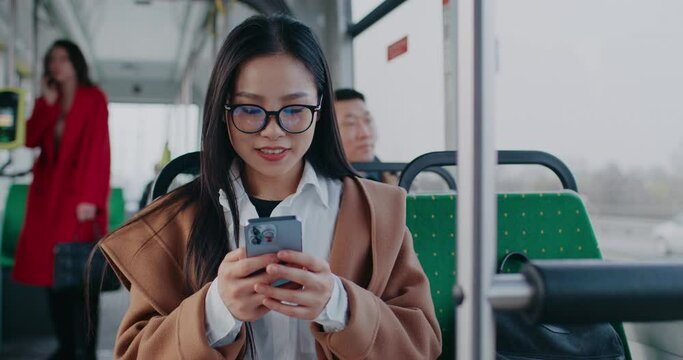 Young Chinese woman sitting in moving train. Scrolling social media or web browser. Acting very surprised from incoming call from relative or boyfriend. Beginning active conversation.