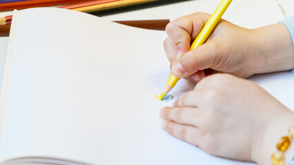 Close-up of a child's hands drawing with colored pencils. Children's creativity and development, fine motor skills, learning to write and draw.