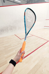 squash racket in the hands of an athlete on the background of a squash court