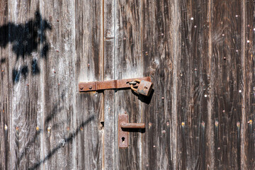 A rusty old padlock on a brown double-leaf wooden door