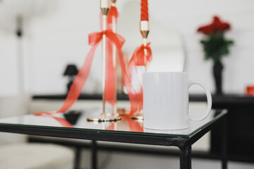 White mug and red candles on a table in a living room.