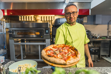 Chef holding fresh pizza in kitchen, chef in salad green uniform in the kitchen. High quality photo