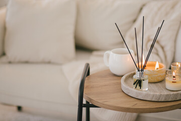 Still life with white mug, aromatic sticks and candles on a table in a cozy living room.