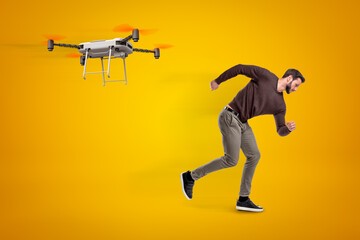 Young man in casual clothes running from camera drone that chases him on amber background.