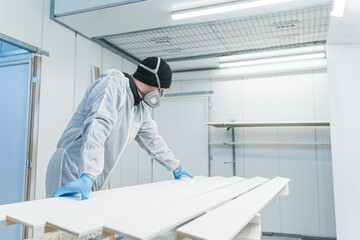 a carpenter with uniform and mask in the process of spraying wooden pieces, workshop. High quality photo